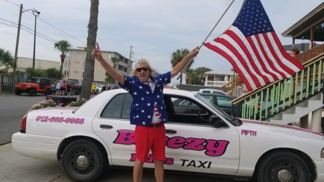 A man standing next to a police car with an american flag.